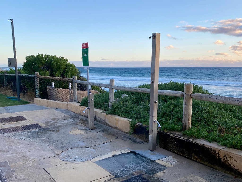 one tall shower and one small shower on a paved area outside near the ocean