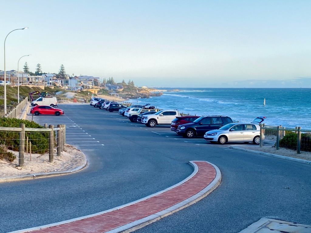 Mettams Pool parking area with several cars parked. it is next to the beach and ocean with buildings in the background