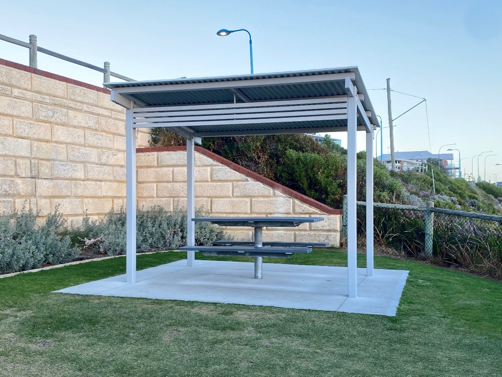 a picnic bench under a shade cover on concrete surrounded by a small grass area